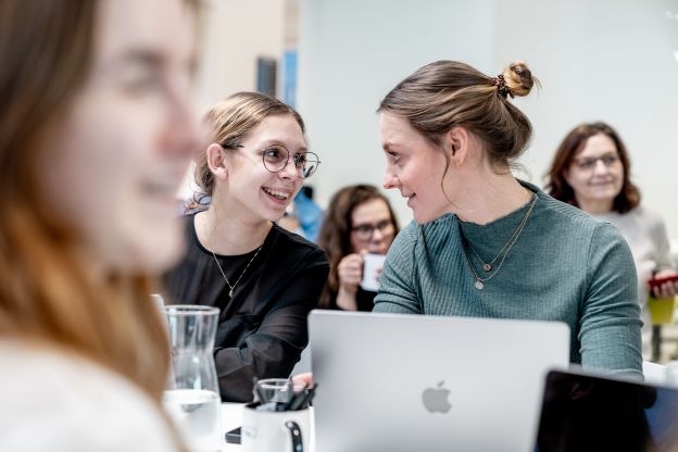 Unsere Kolleginnen Franzi und Fabienne sitzen vertieft in ein Gespräch vor ihren Laptops.