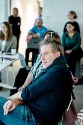 Mehrere Personen sitzen aufmerksam in einem Veranstaltungsraum und hören zu.