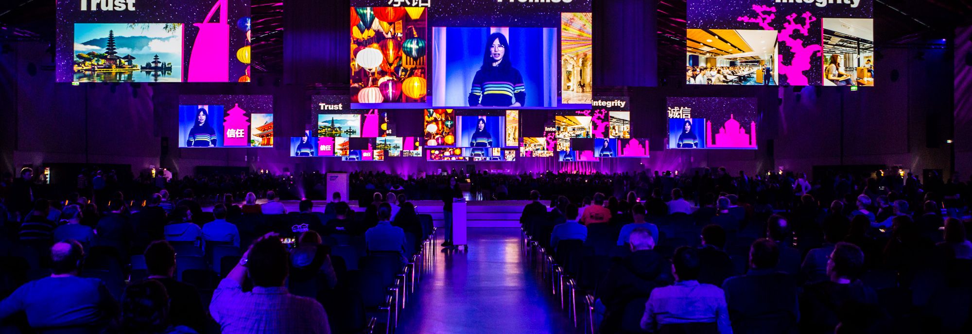 Bühne mit moderner Lichtshow bei einem Event, großes Publikum blickt auf mehrere LED-Screens.