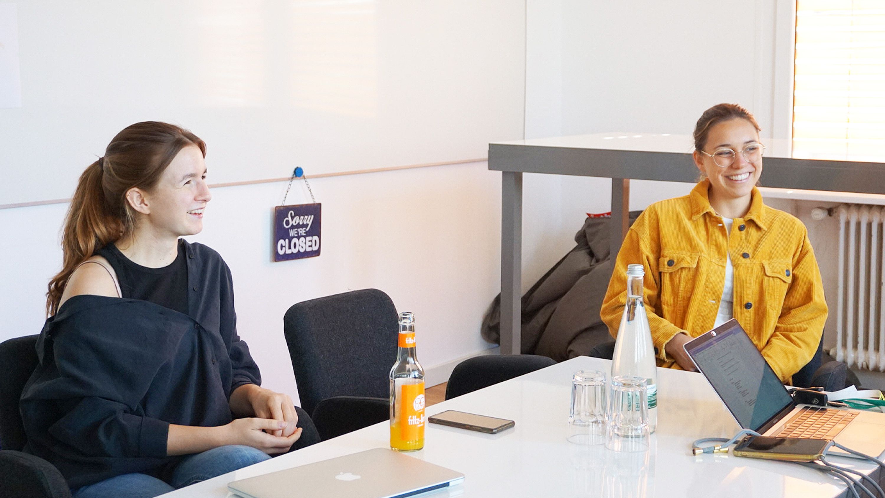 Neue ottomisu Mitarbeiterinnen Claudia und Elly, die an einem Tisch sitzen und sich mit Kolleg*innen unterhalten