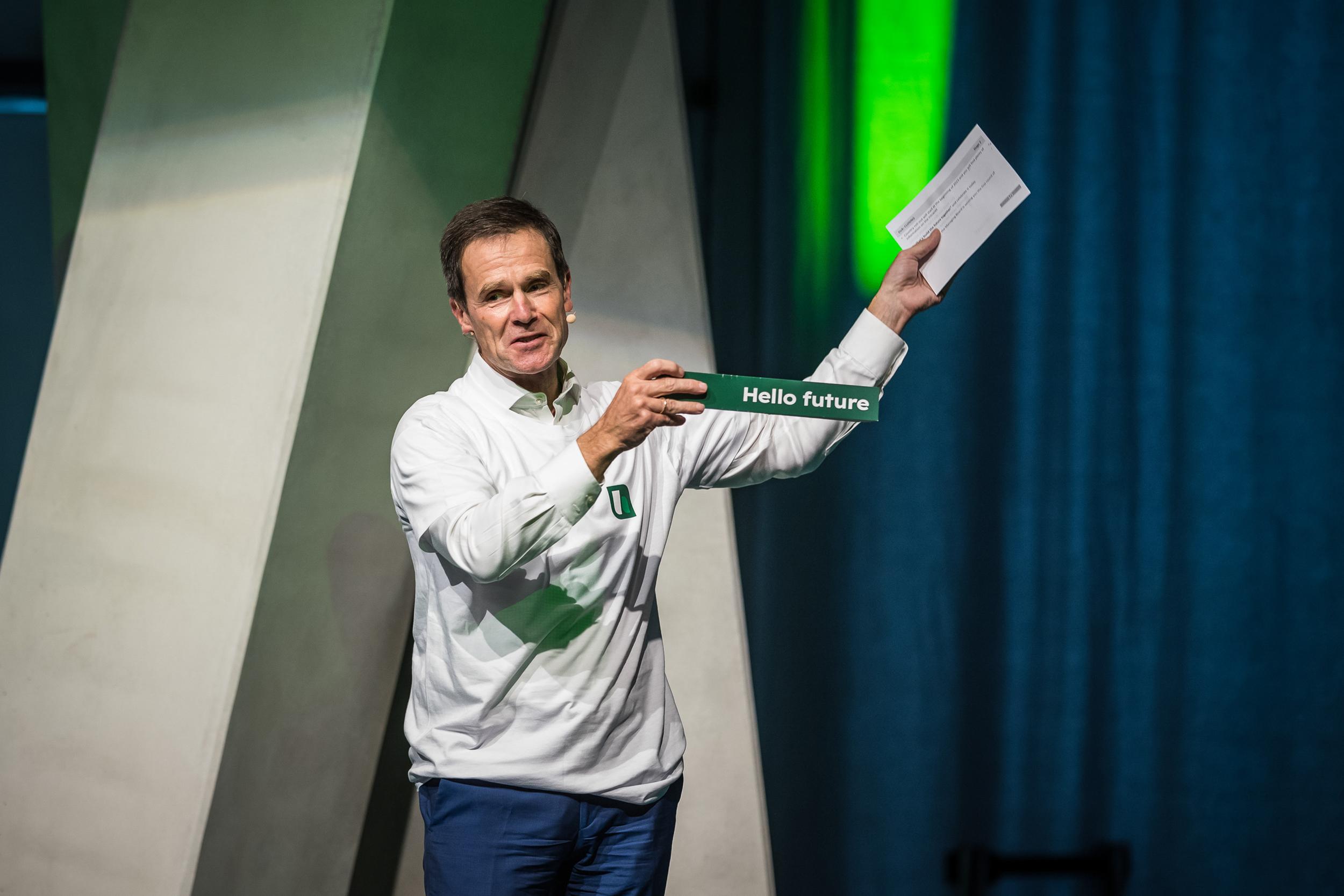 Dr. Dominik von Achten mit Mikrofon auf einer Bühne mit grünem Licht - motivierende Körpersprache.