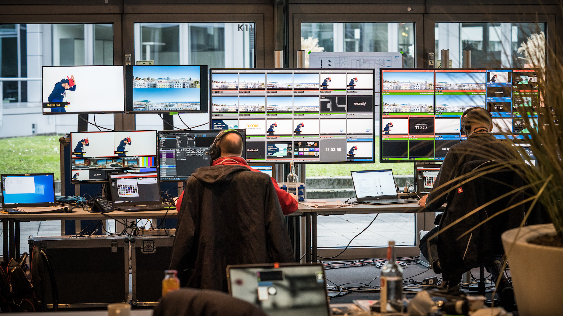 Zwei Personen sitzen vor großen Monitorwänden in der Regie. Zu sehen sind mehrere Kamerabilder, Live-Grafiken und Schnittsoftware