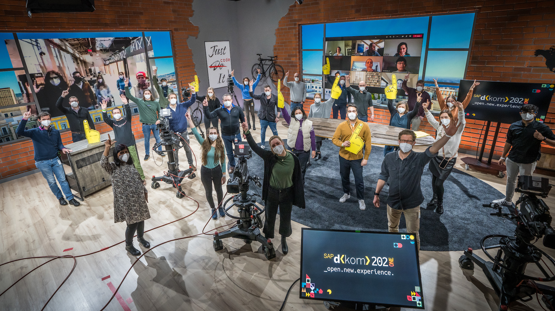 Gruppenfoto mit allen Beteiligten in einem Studio-Set. Kamerateam, Technikcrew und Moderator:innen feiern gemeinsam vor der virtuellen Bühne