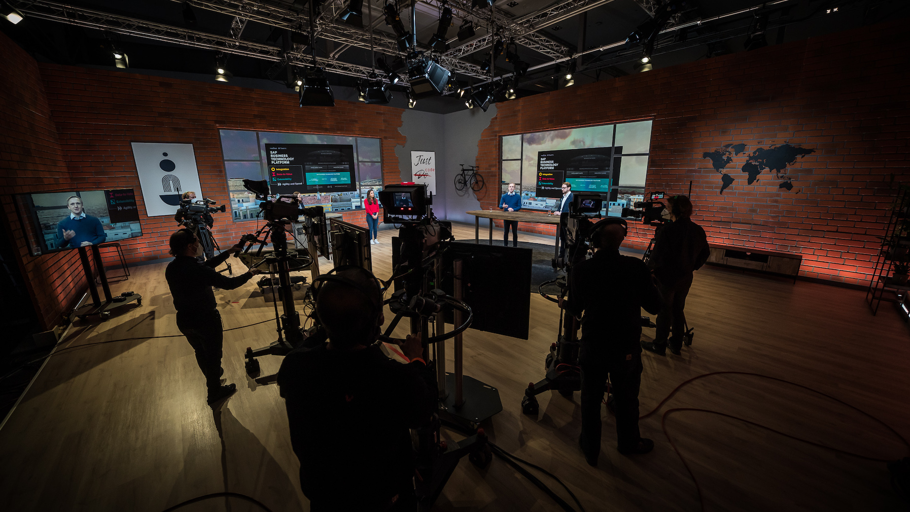 Dunkel ausgeleuchtetes Studio mit mehreren Kameras, Technikteam und Live-Sendung auf Monitoren im Hintergrund. Das Team arbeitet konzentriert in einer professionellen Produktionsumgebung