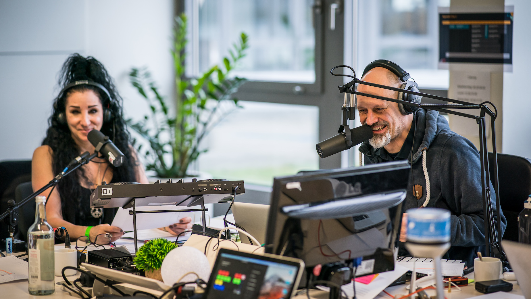 Zwei Moderatoren im Radiostudio mit Headsets und Mikrofonen.