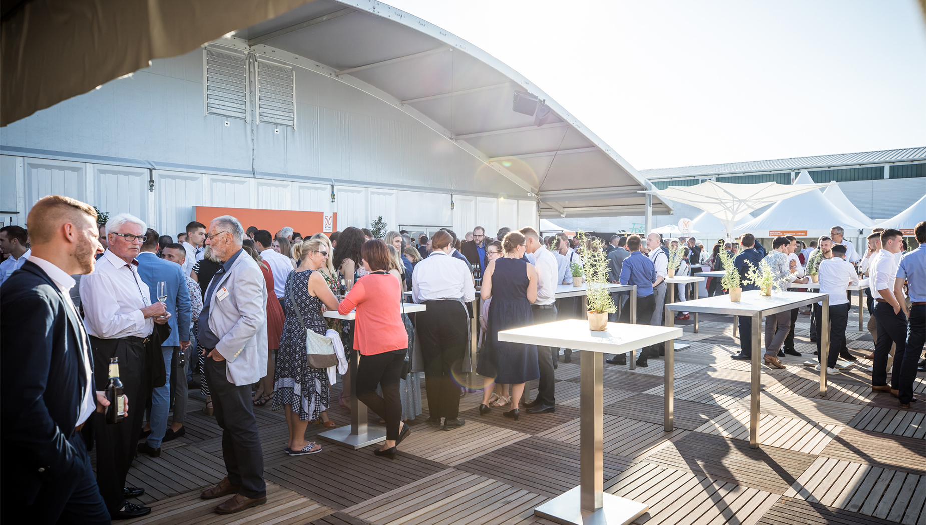 Zahlreiche Gäste in sommerlicher Atmosphäre bei einem Outdoor-Empfang mit Stehtischen und lockerer Stimmung.