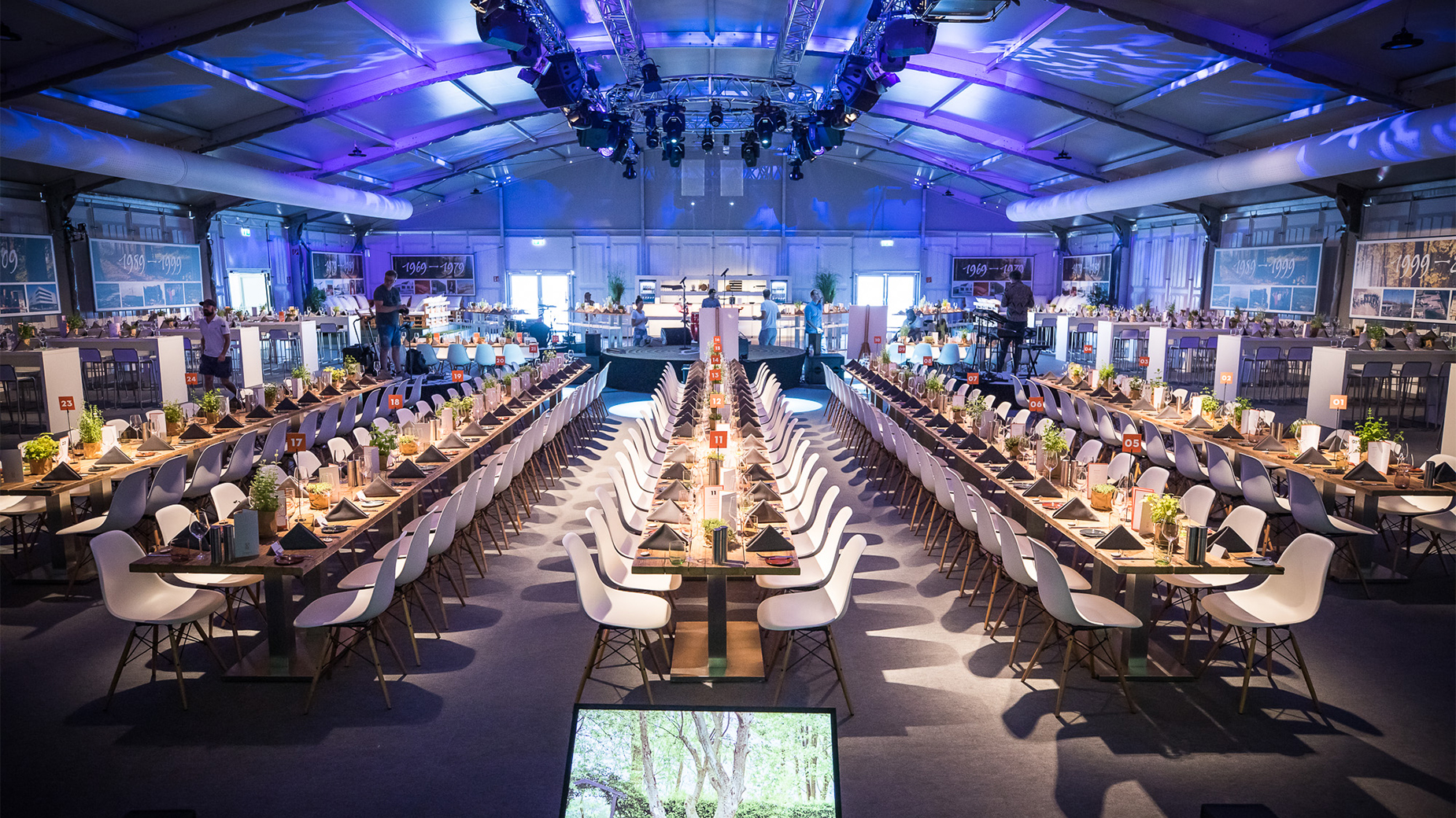 Große, stimmungsvoll beleuchtete Eventhalle mit langen Bankett-Tafeln und Bühne.