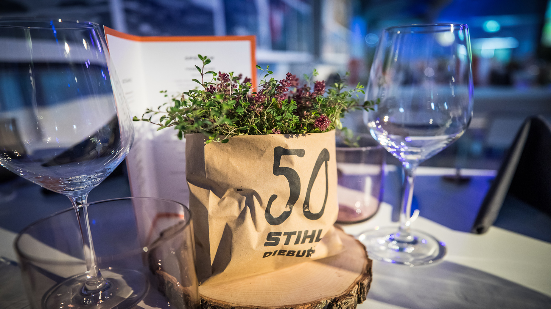 Detailaufnahme eines gedeckten Tisches mit Kräuterpflanze im Papiertopf „50 STIHL Dieburg“.