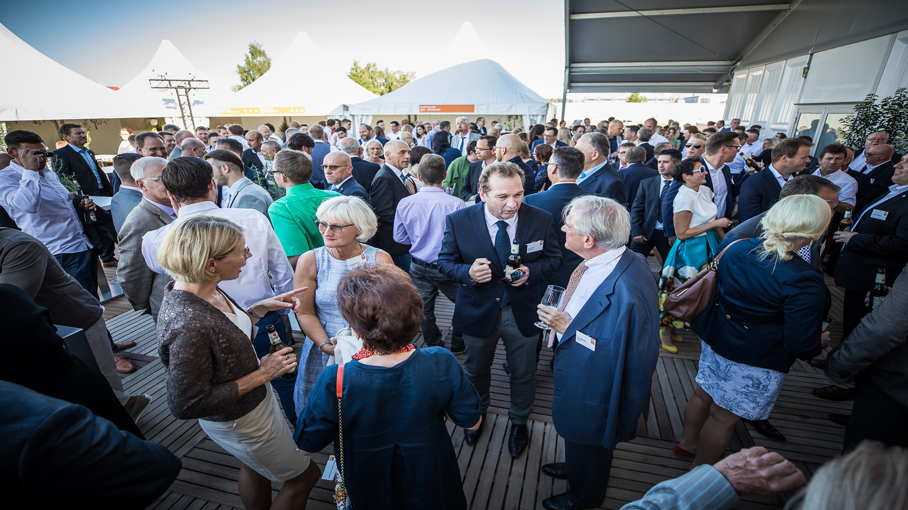 Große Gästegruppe beim Austausch auf der Terrasse mit lockerer Businesskleidung.