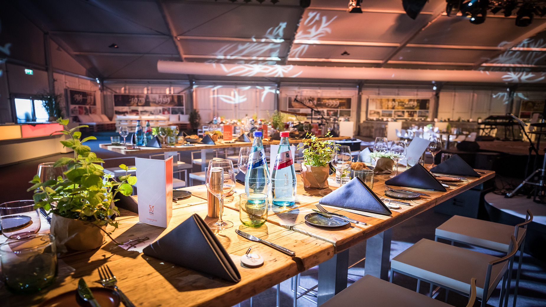 Stilvoll gedeckter Tisch mit Wassergläsern, Besteck, Menükarte und Kräuterdeko.