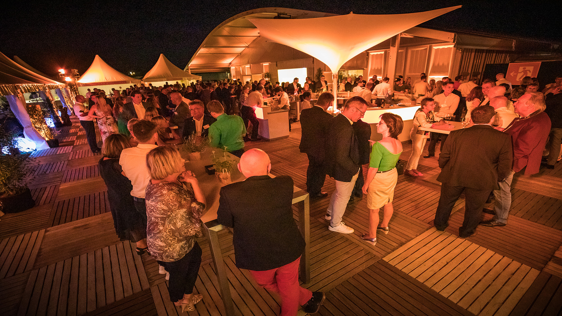 Geselliges Zusammensein unter Zeltdächern bei Nacht mit stimmungsvoller Beleuchtung.