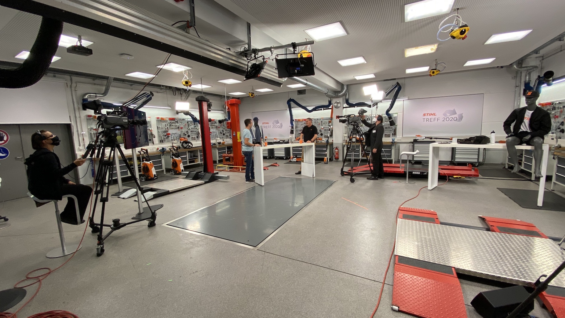 Kameraaufnahme in einem Labor- oder Technikstudio mit zwei Personen vor einem Arbeitstisch, ein Kameramonitor zeigt die Szene live.