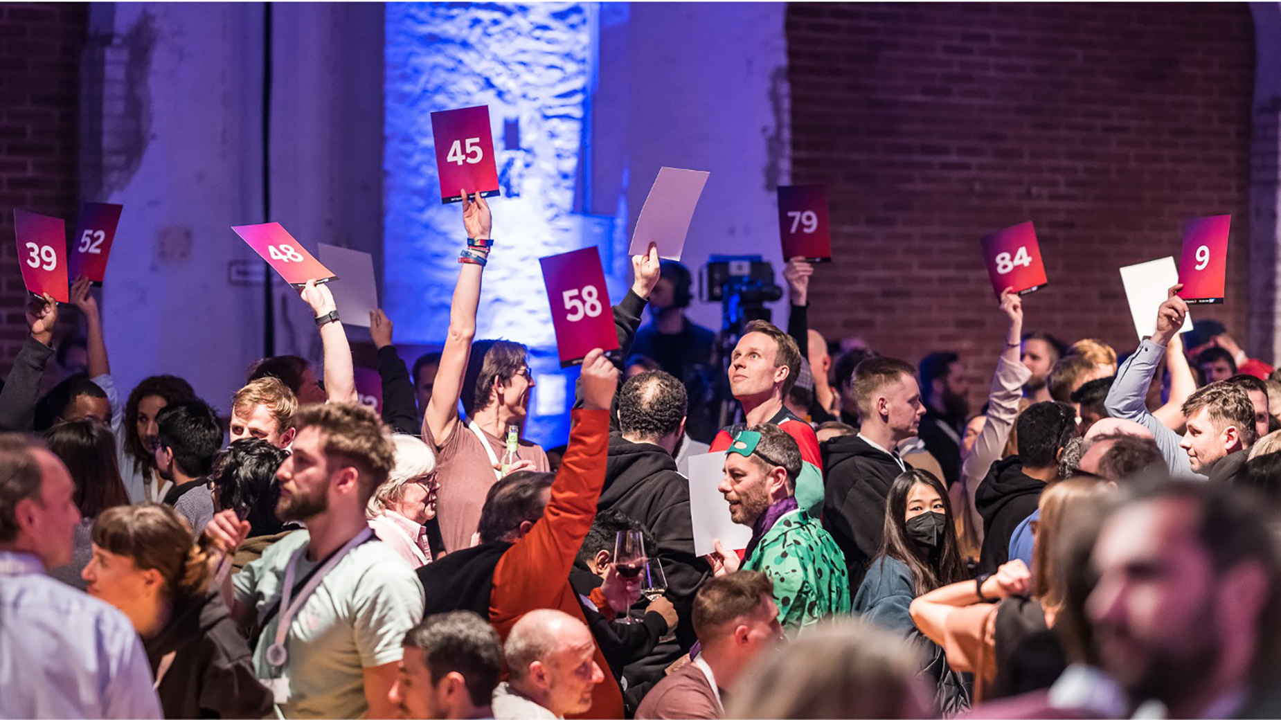 Teilnehmende halten rote Abstimmungskarten in die Luft, dynamische Szene mit erhobenen Händen.