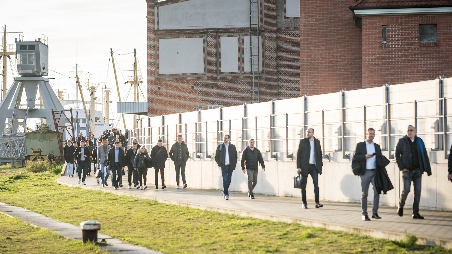 Zu sehen sind die Besucher*innen, die sich auf den Weg in die Location machen. Im Hintergrund ist der Hamburger Hafen erkennbar.