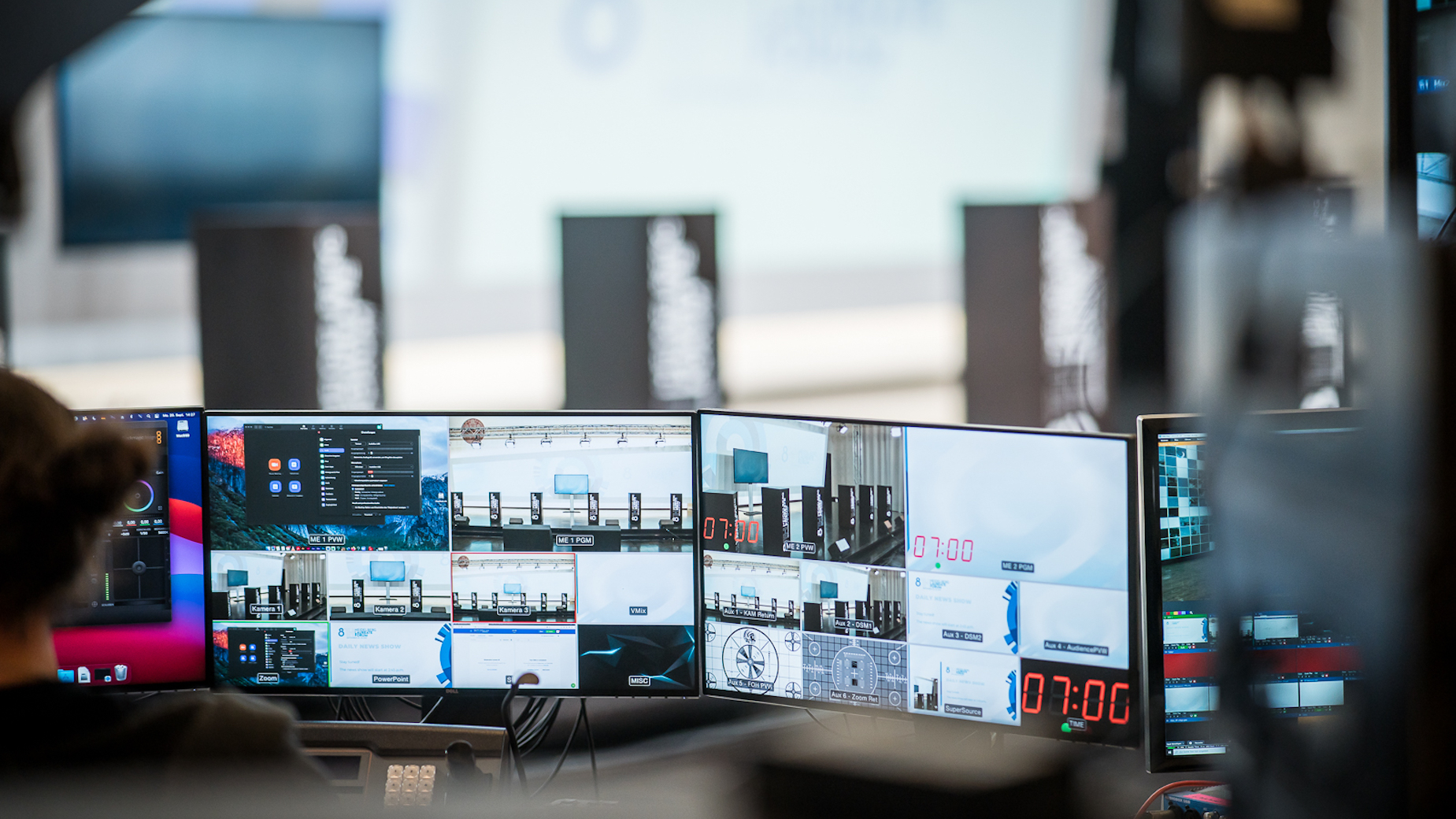 Mehrere Bildschirme mit verschiedenen Live-Feeds, Schnitt-Tools und Countdown-Zeiten in einer technischen Produktionsumgebung.