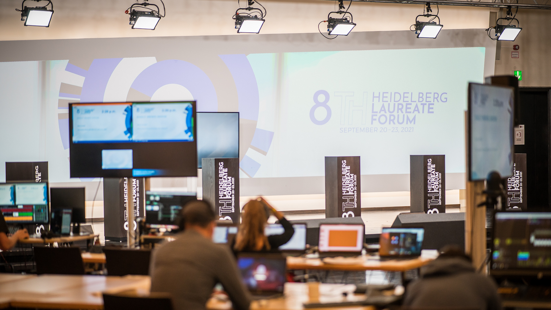 Blick in den Veranstaltungsraum des 8th Heidelberg Laureate Forum mit leerer Bühne, mehreren Monitoren und Regiearbeitsplätzen im Vordergrund. Auf der Leinwand steht das Veranstaltungsdatum: 20.–23. September 2021.