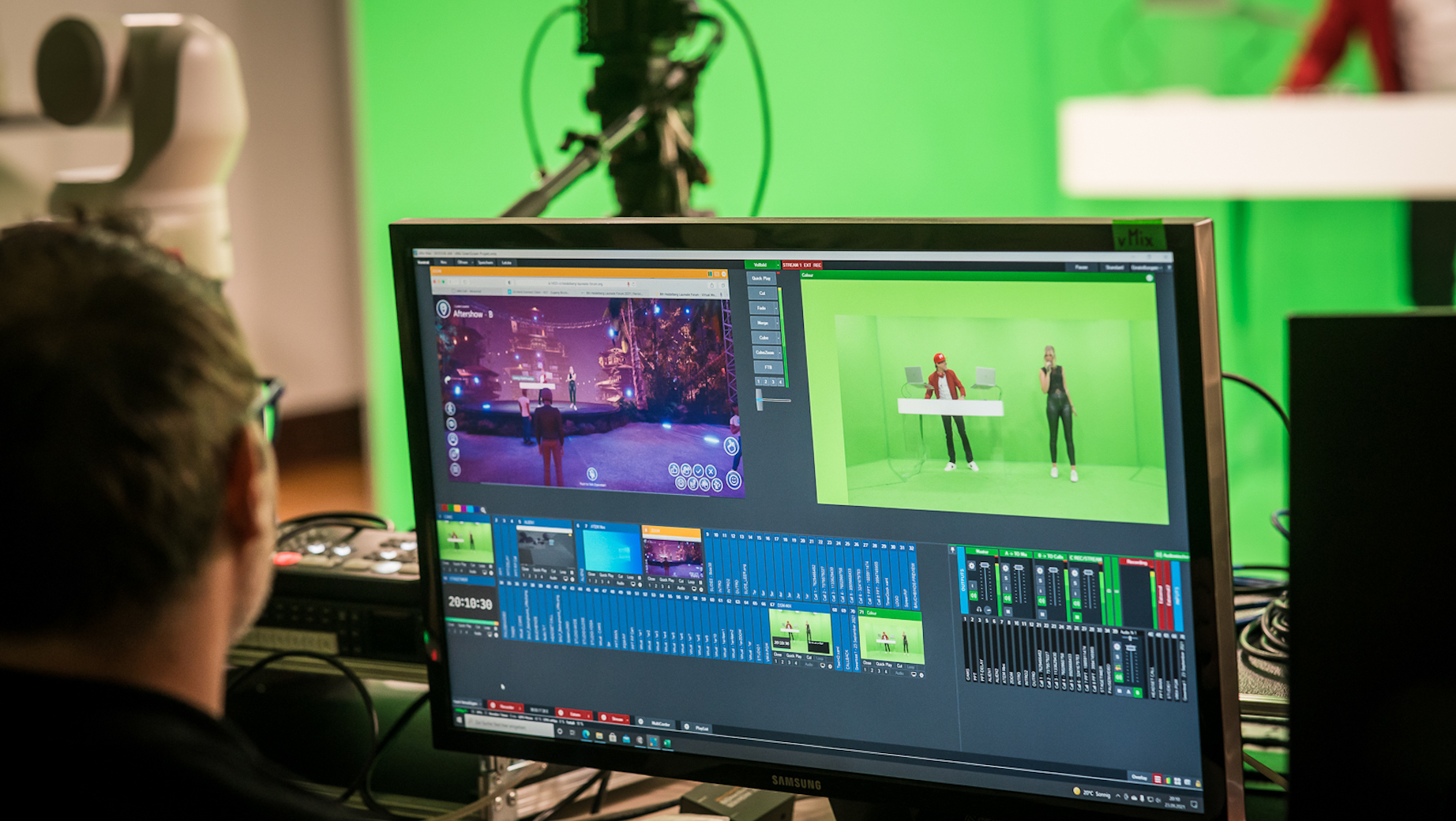 Techniker betrachtet zwei Screens mit Live-Übertragung: links die virtuelle Bühnenkulisse, rechts das Greenscreen-Bild mit DJ und Sängerin.