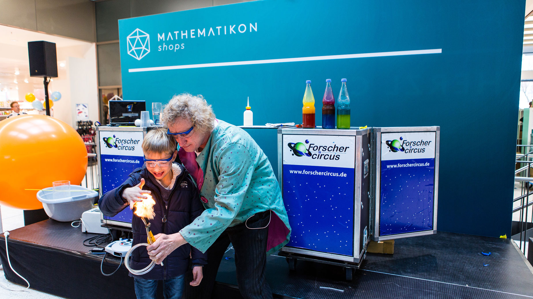 Moderator zeigt einem Kind bei einer Mitmach-Experimenteshow ein wissenschaftliches Phänomen auf der Bühne des Mathematikon-Events.