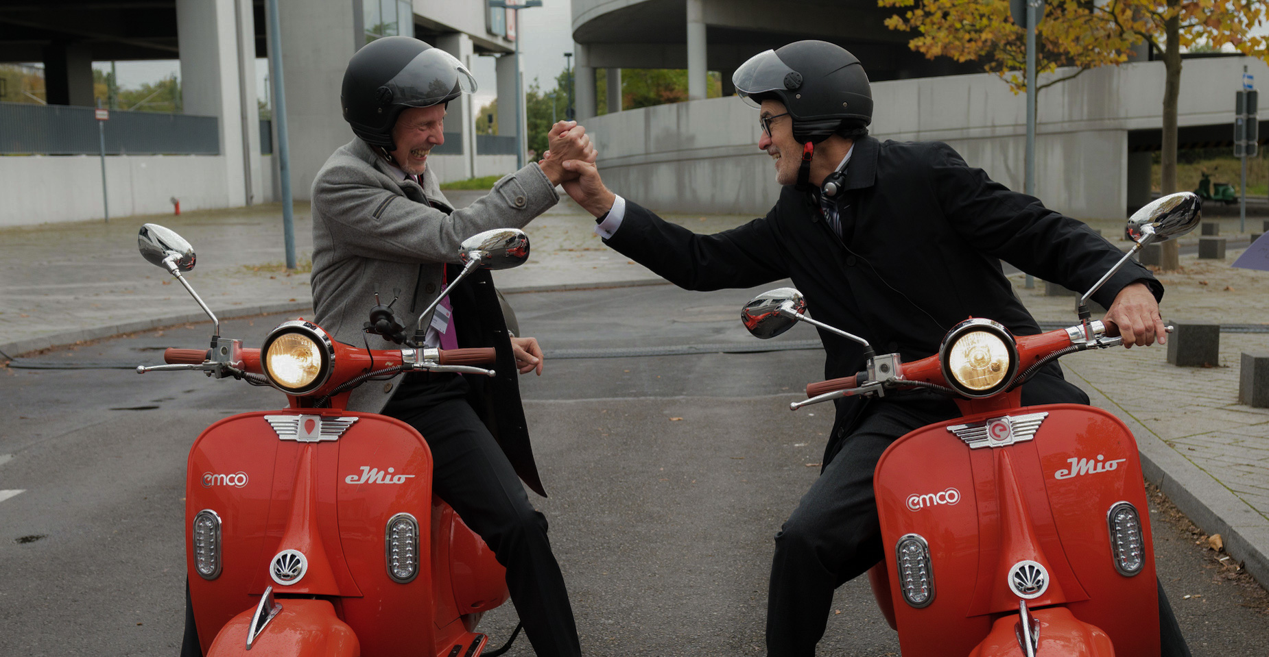 Zwei Personen auf roten Rollern treffen sich zum High-Five – Symbol für Mobilität und Teamspirit.