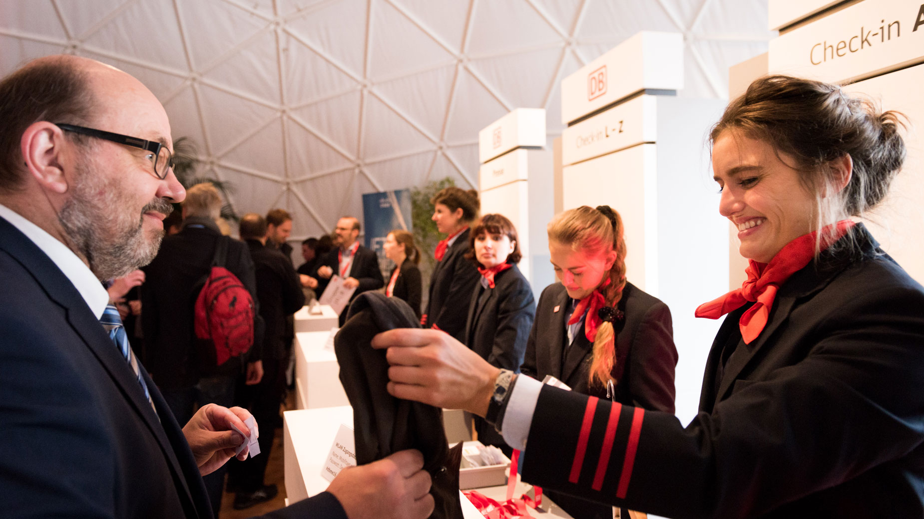 Empfangssituation auf einem Event – eine Hostess begrüßt einen Teilnehmer mit einem Willkommensband.