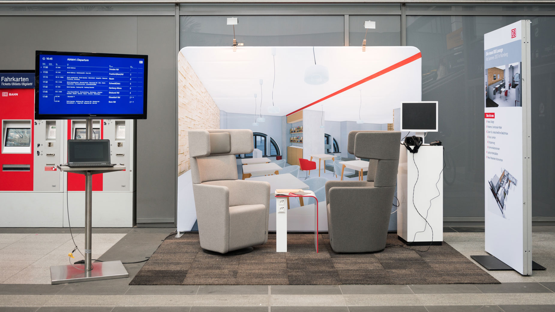 Ausstellungsbereich mit modernen Sitzmöbeln, Touchscreen und Abflugtafel – Fokus auf Mobilitätsdesign.