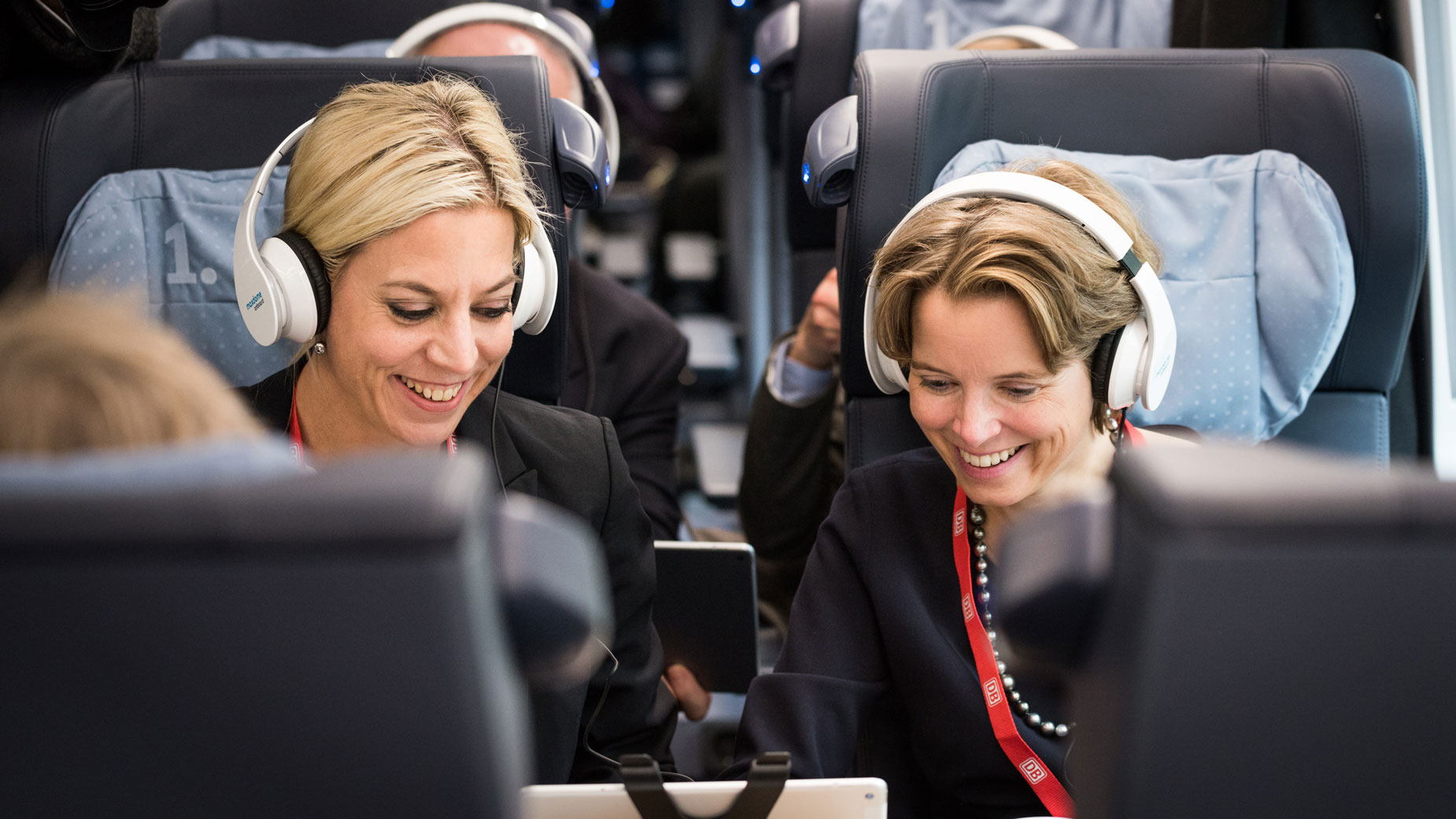 Zwei Frauen mit Kopfhörern in einem Zug, konzentriert bei einem gemeinsamen Audioprogramm.