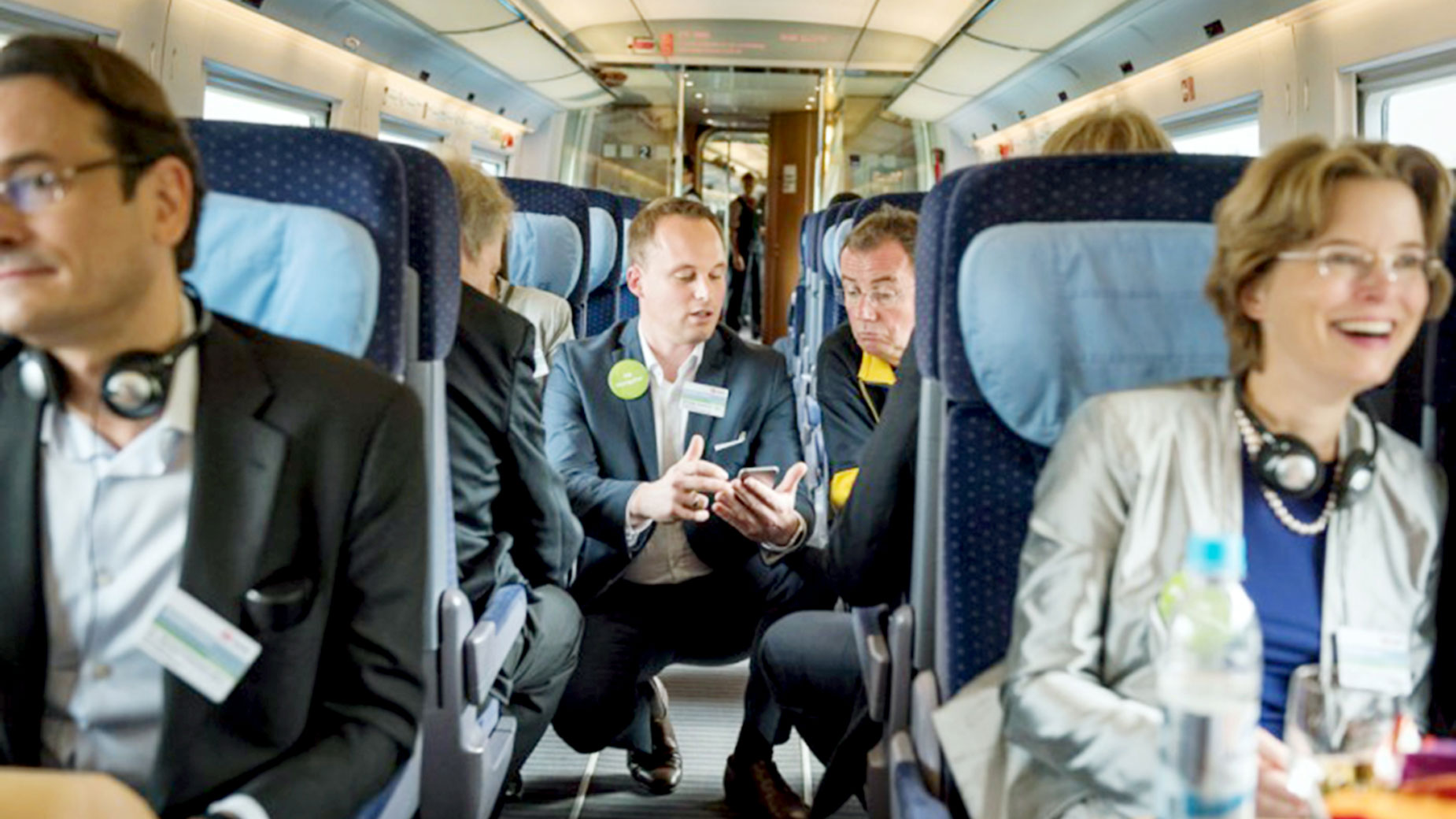 Teilnehmende einer Mobilitätsveranstaltung sitzen mit Kopfhörern in einem fahrenden Zug.