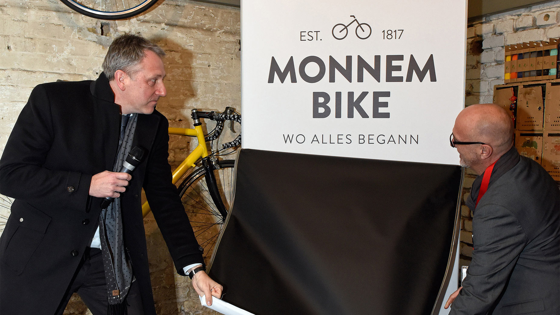 Offizielle Enthüllung des Monnem-Bike-Logos durch zwei Vertreter im historischen Ambiente