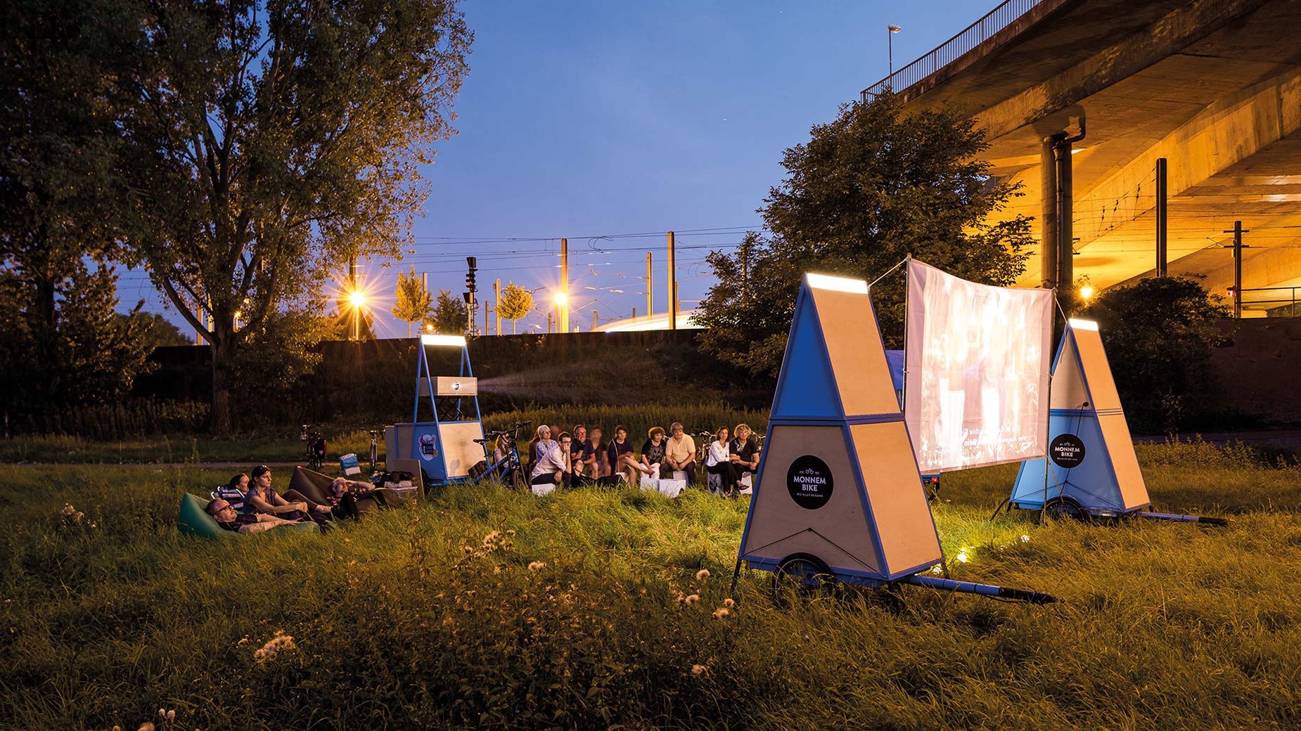 Kreative Lichtinstallation und Fahrradzelte unter einer Brücke als Teil der Monnem-Bike-Aktivitäten.