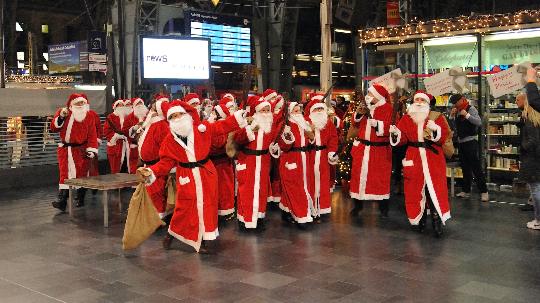Zahlreiche als Nikolaus verkleidete Menschen singen und tanzen auf dem Bahnsteig des Frankfurter Hauptbahnhofes.