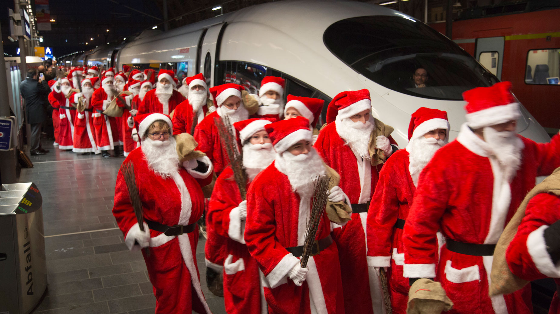 Zahlreiche als Nikolaus verkleidete Menschen laufen auf dem Bahnsteig.