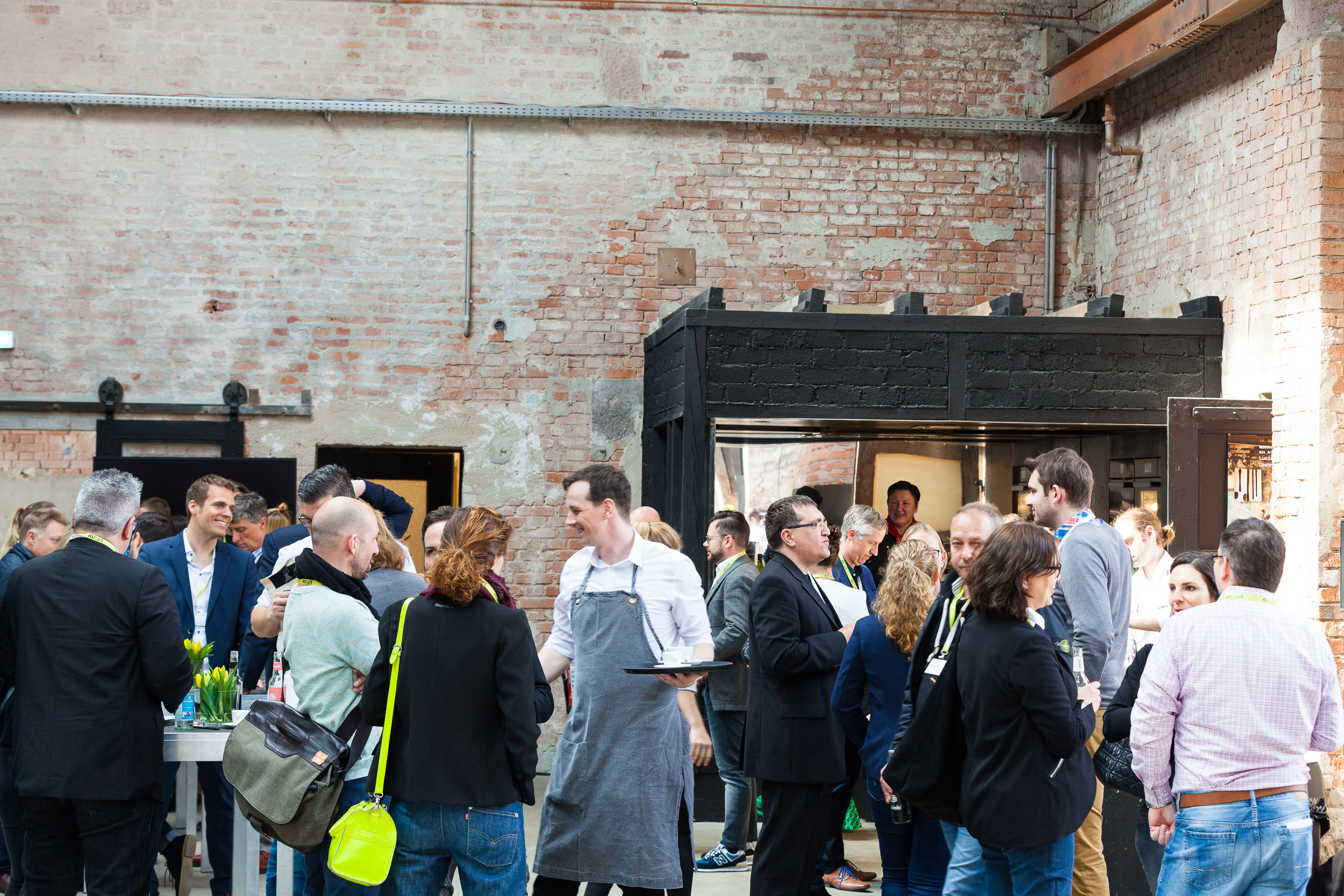 Besuchergruppe steht im Außenbereich vor einer alten Backsteinhalle, angeregte Gespräche bei Sonnenschein.