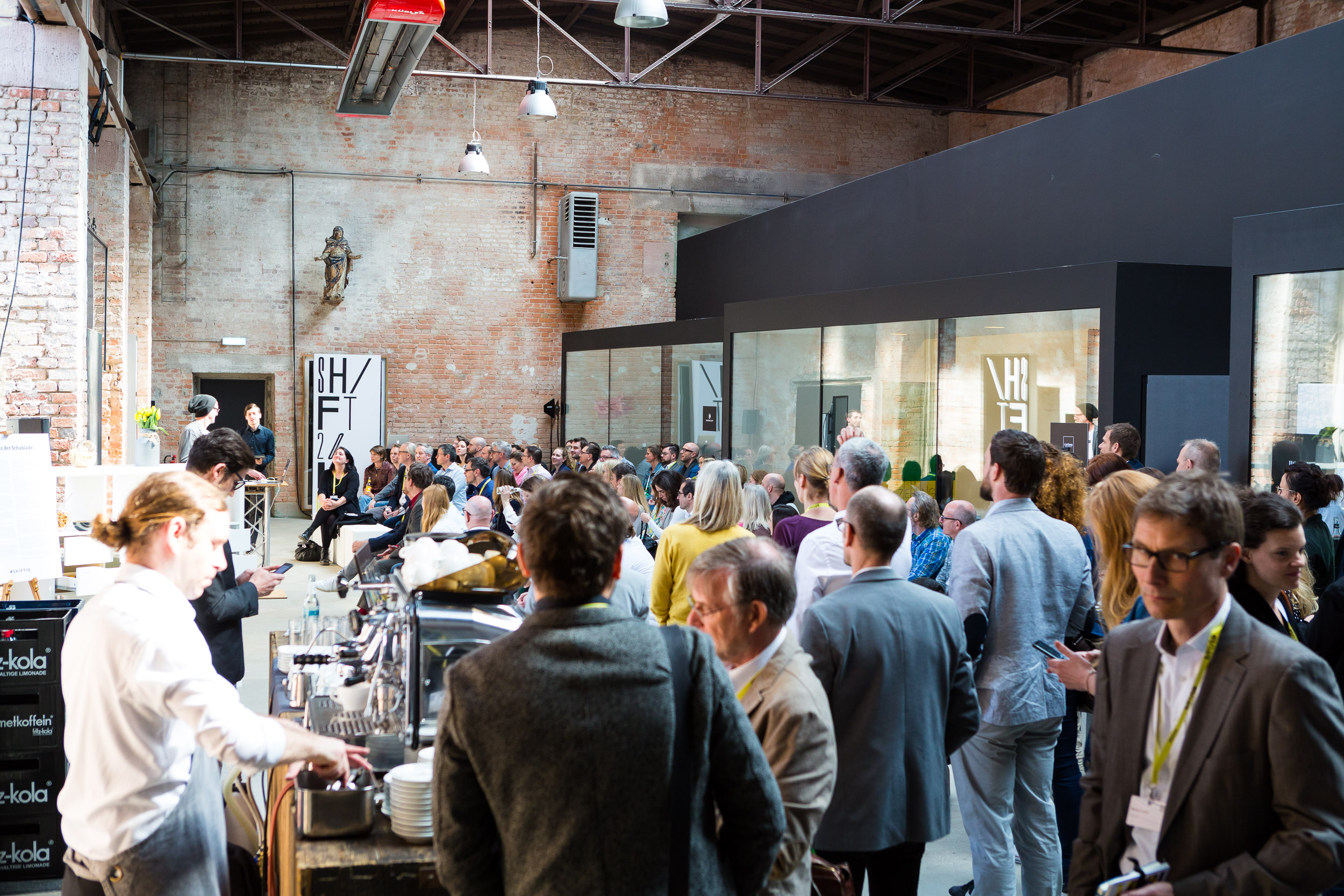 Viele Gäste im Gespräch in einer Industrie-Location mit urbanem Charme, lebendige Networking-Atmosphäre.