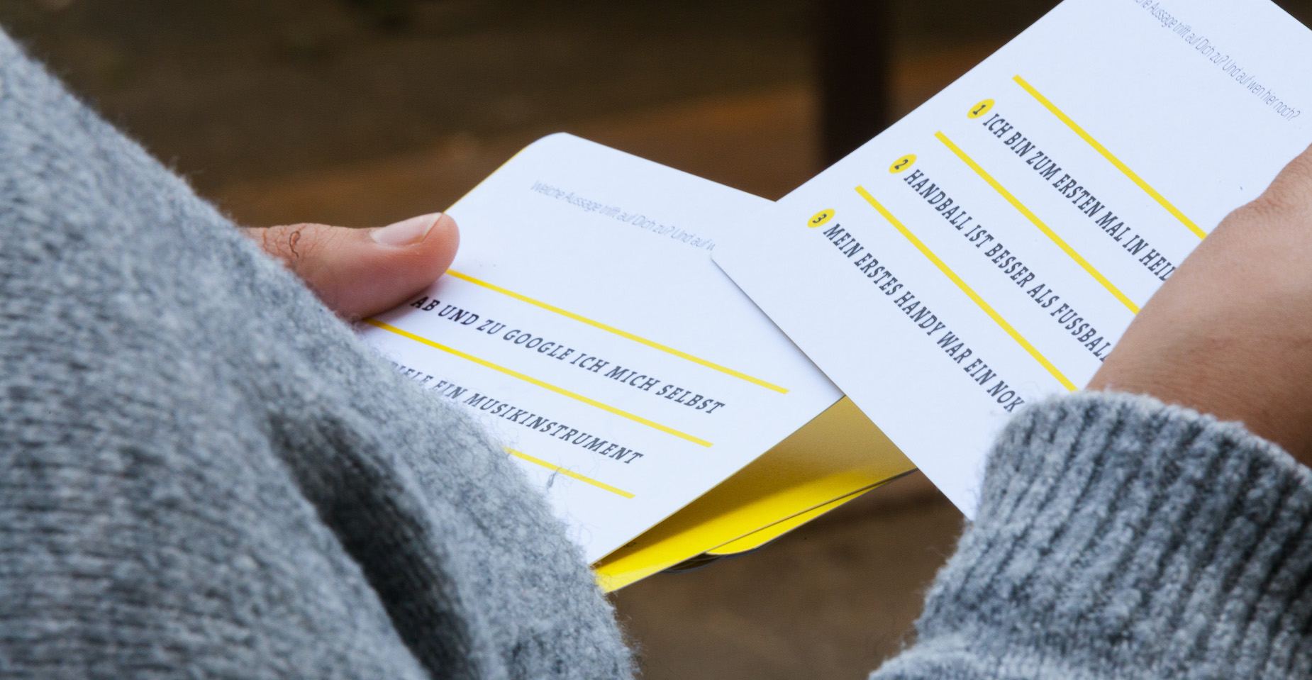 Person mit grauem Pullover liest ein gefaltetes Veranstaltungsprogramm mit farbigen Markierungen.