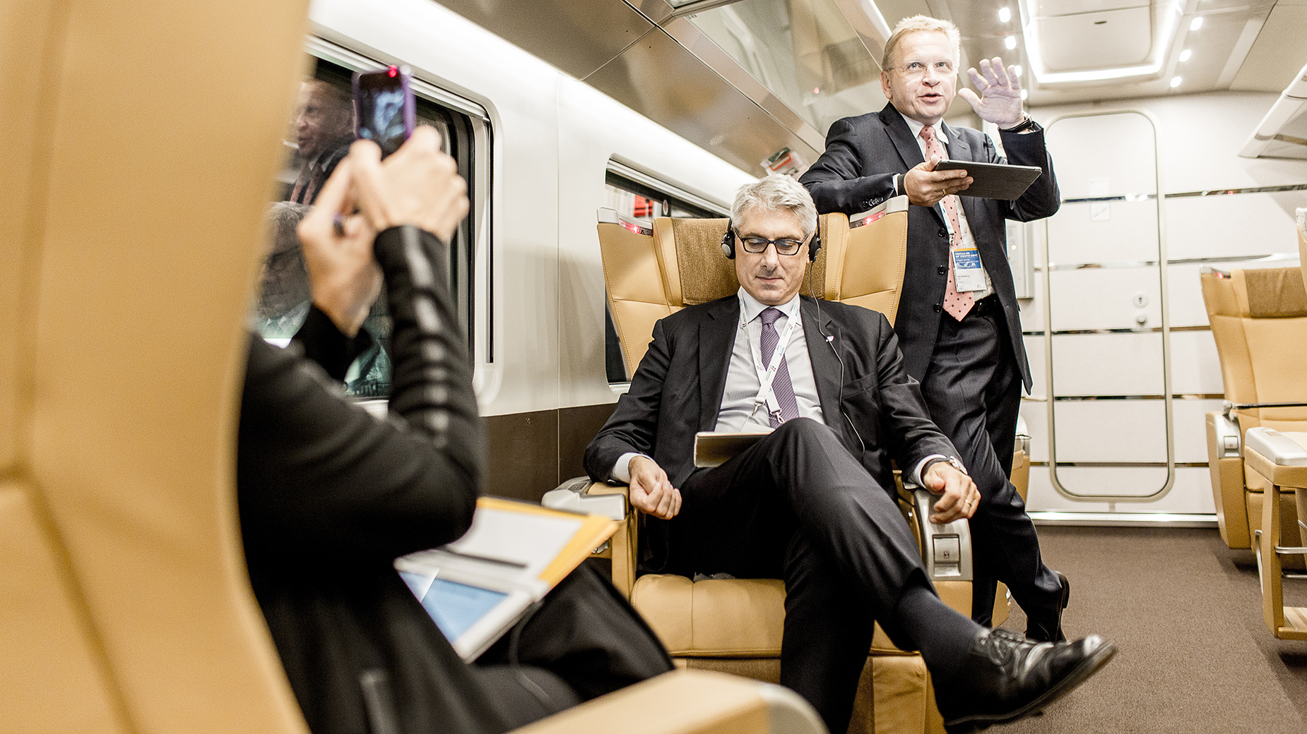 Business-Männer im Austausch in einer komfortablen Zug-Sitzgruppe mit goldfarbenen Sitzen.