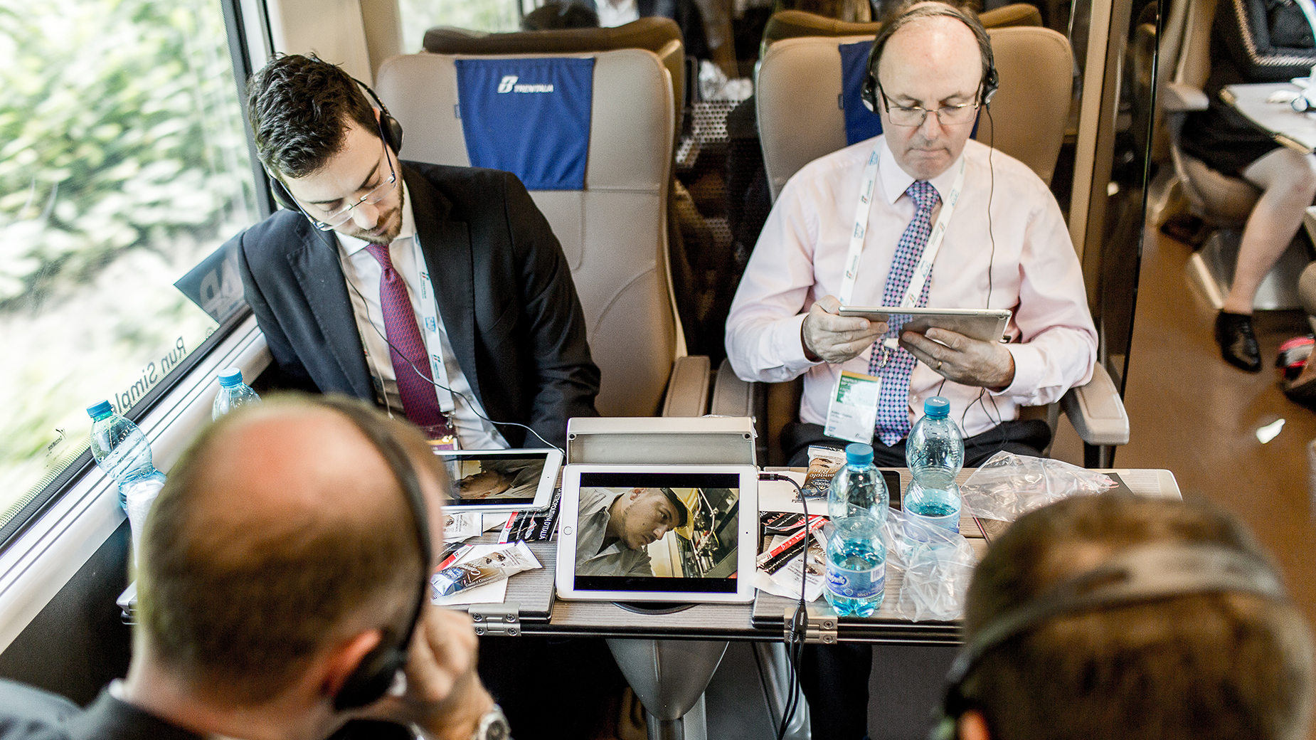 Zwei Männer mit Laptops im Bordbüro eines ICE-artigen Zuges bei der Arbeit.