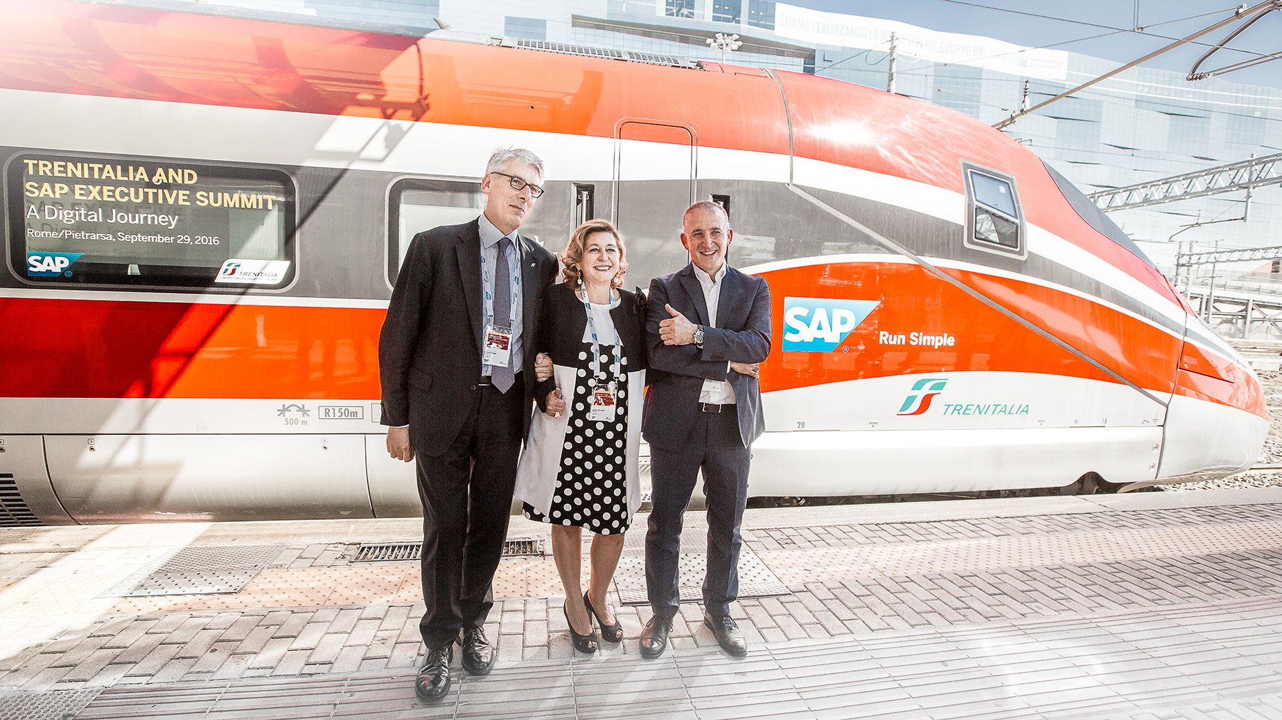 Drei Personen in Businesskleidung posieren vor einem modernen, rot-weißen Zug.