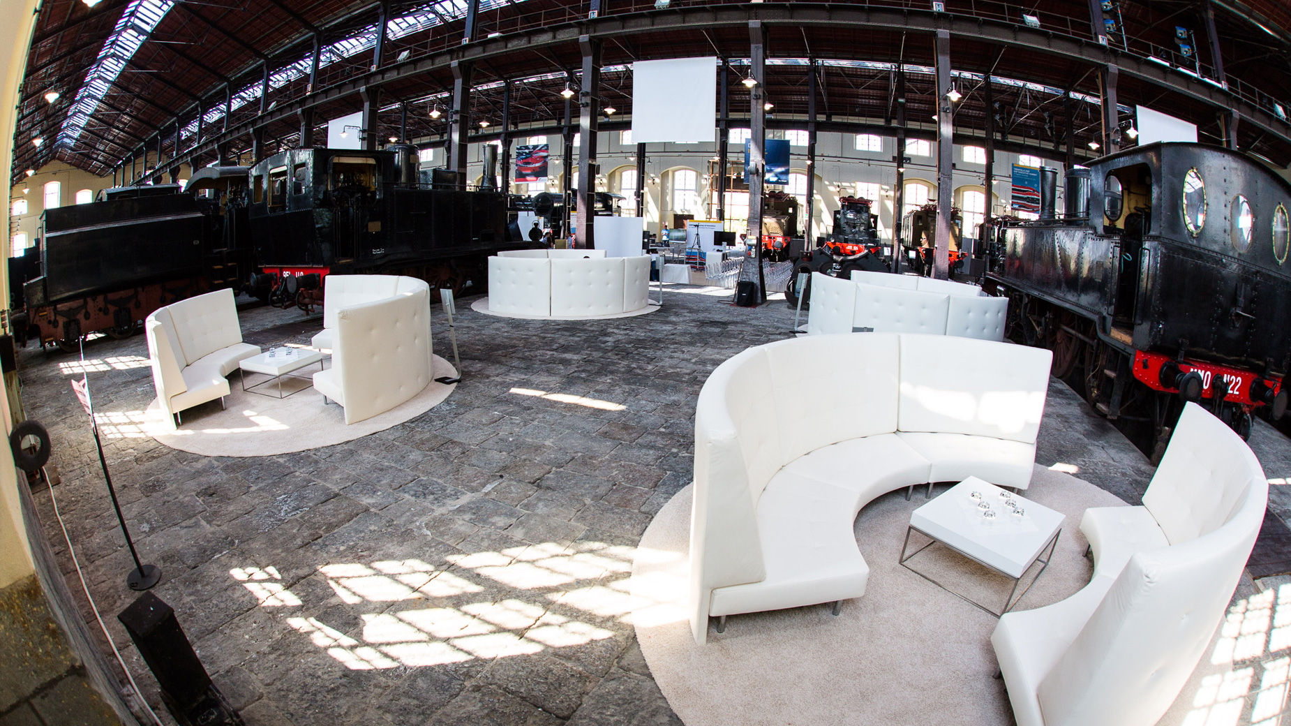 Offene Eventfläche mit weißen Loungemöbeln unter Tageslicht in historischer Halle.
