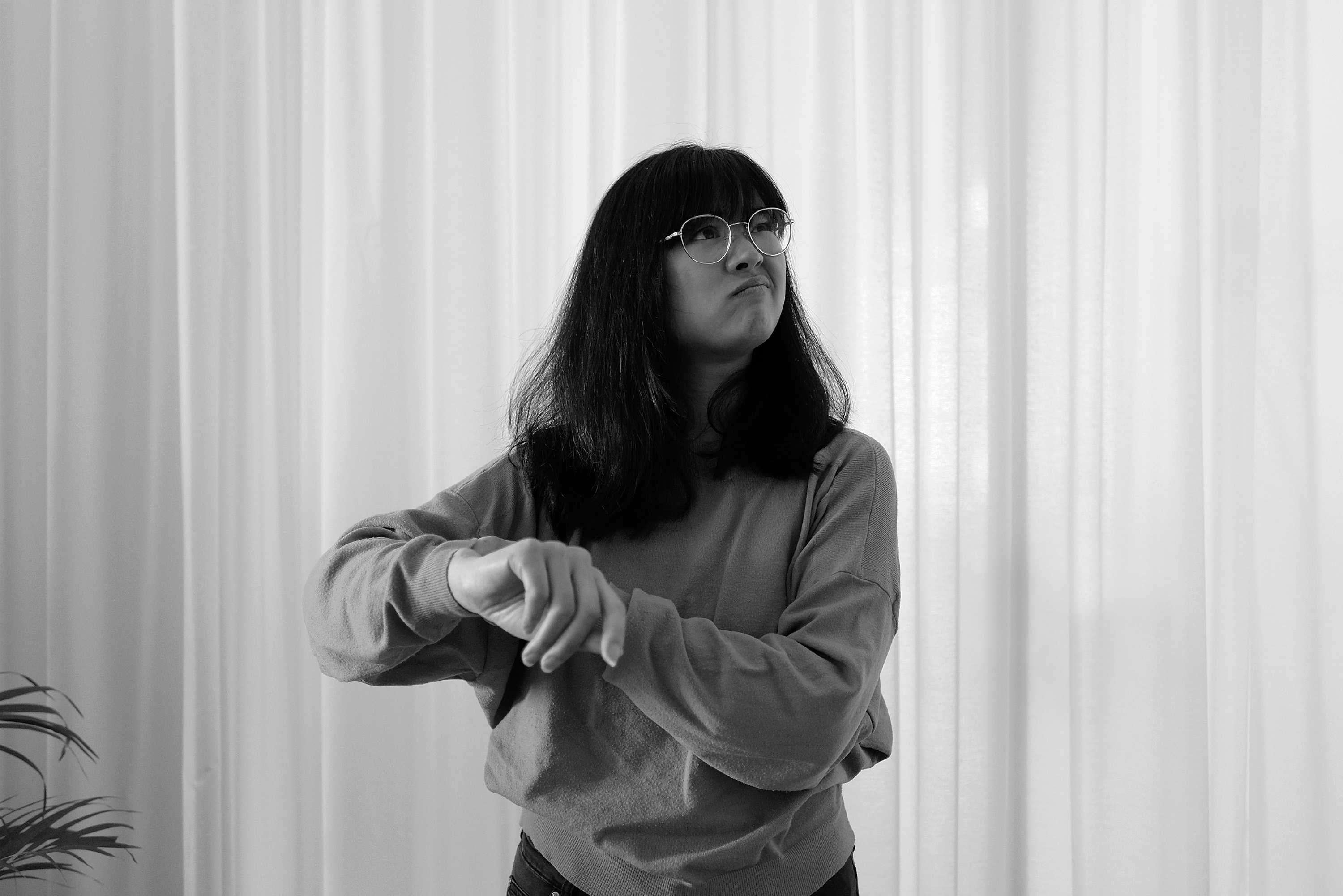 Schwarz-weiß Fotografie von Anita, die verwirrt nach rechts schaut und mit ihrem Finger auf ihr Handgelenk zeigt, als würde sie dort eine Uhr tragen