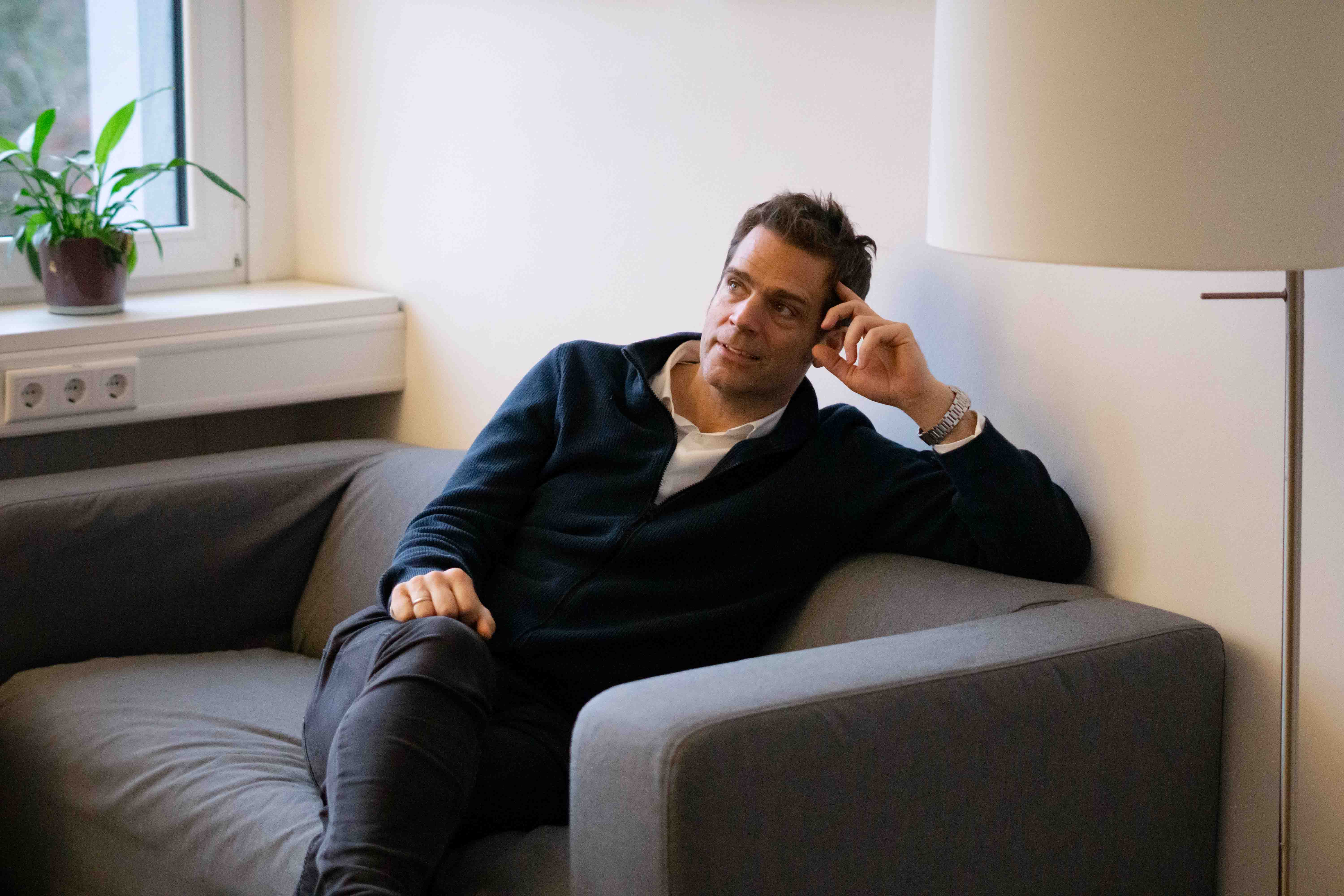 ottomisu CEO Jörn Huber sitzt auf einem grauen Sofa im Büro und führt ein Interview mit Kolleg*innen.