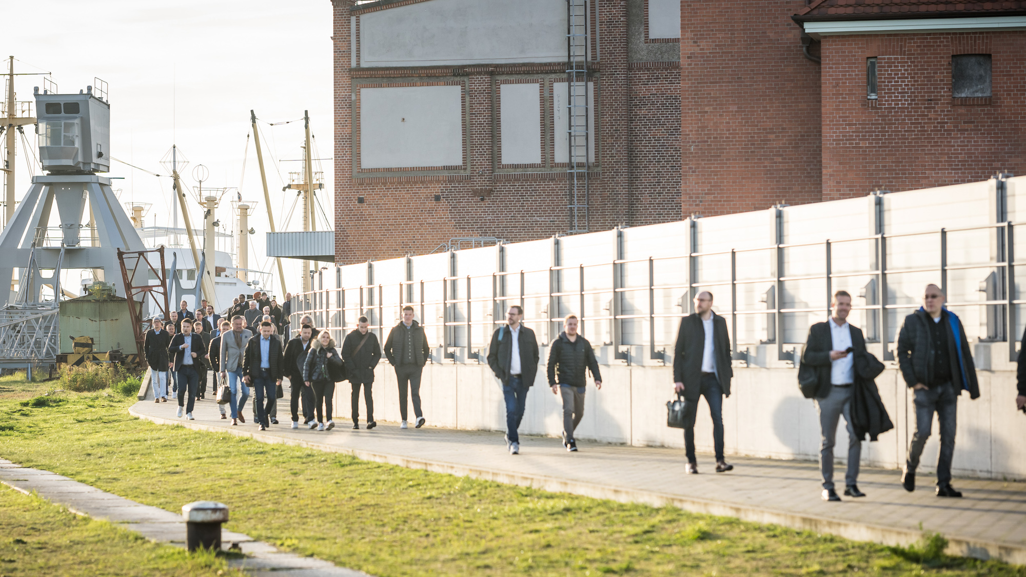 Zu sehen sind die Besucher*innen, die sich auf den Weg in die Location machen. Im Hintergrund ist der Hamburger Hafen erkennbar.