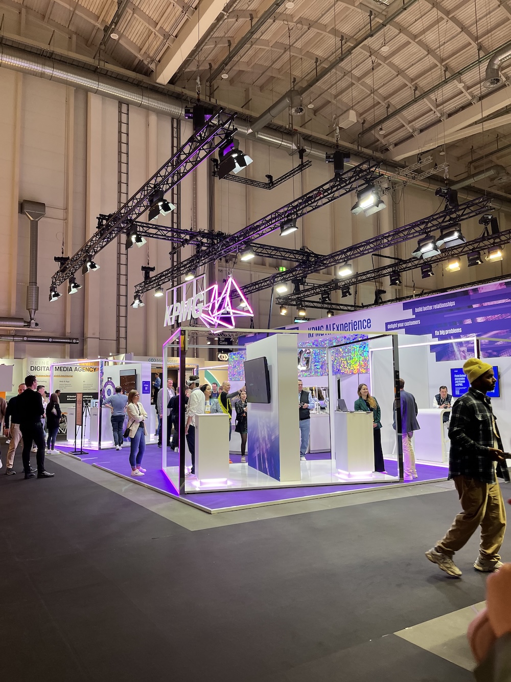 Messestand von KPMG auf der OMR mit futuristischer LED-Installation in lila Licht, Besucher*innen gehen vorbei.