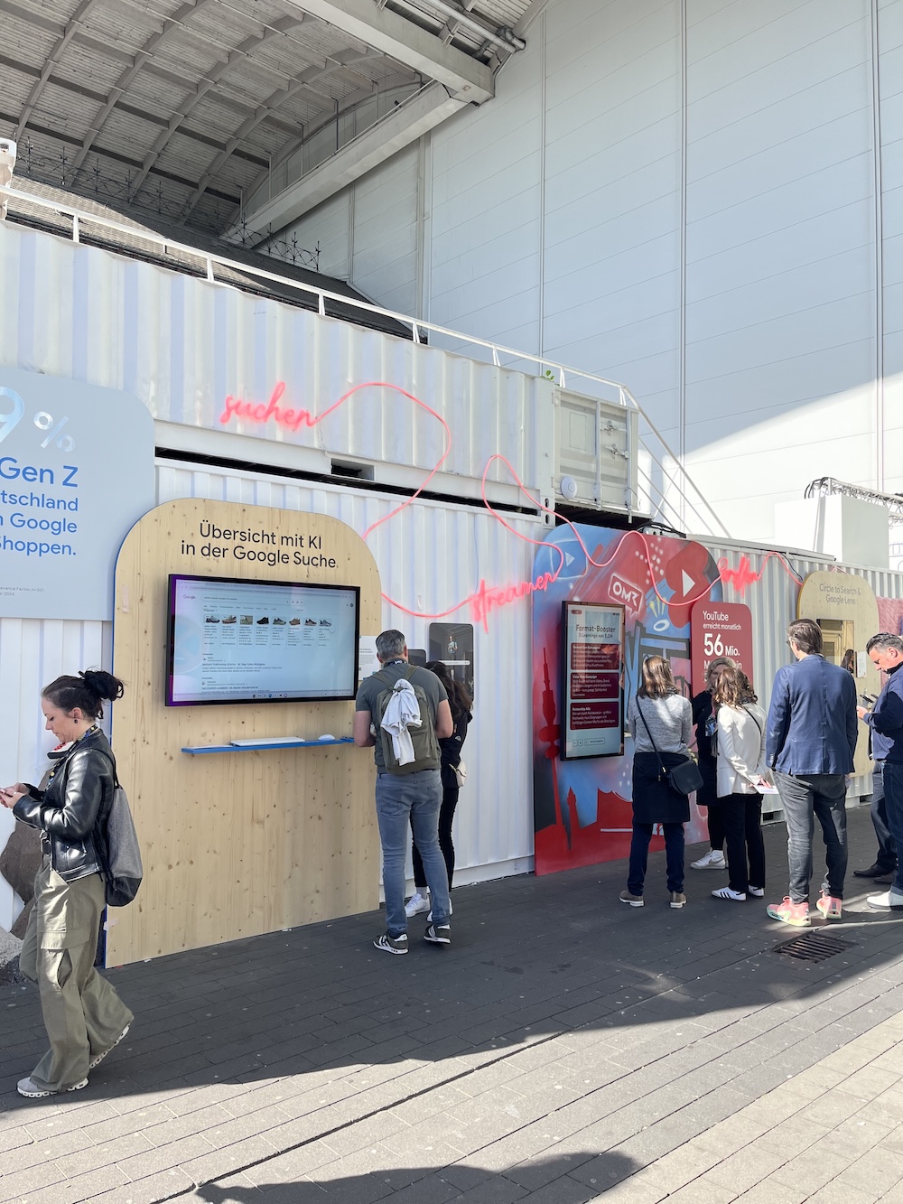 Interaktiver Google-Stand im Außenbereich der OMR mit Containerelementen, Holzverkleidung und Infobildschirmen zum Thema KI und Suche.