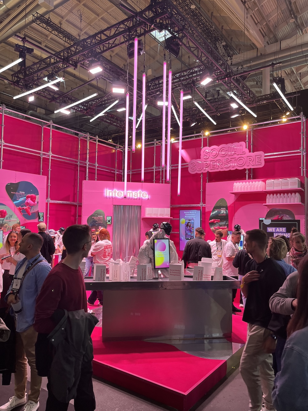 Messestand mit grellpinkem Design und dem Schriftzug „Social Superstore“, viele Besucher*innen umgeben eine zentrale Präsentationsinsel.