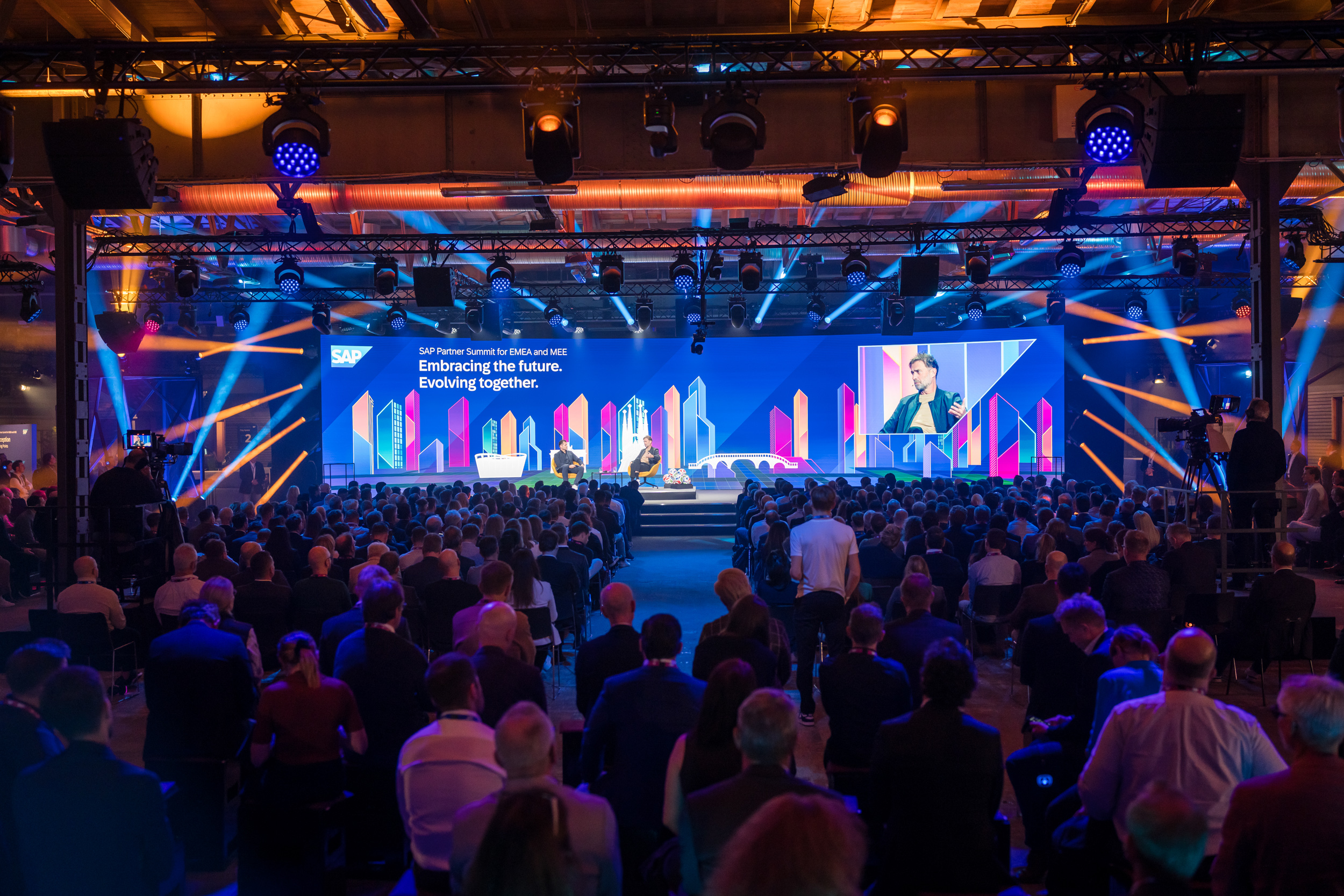 Wide-angle view of the audience during a panel talk on the main stage. Two speakers converse while SAP-branded visuals glow in the background.